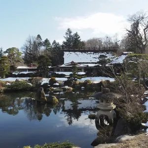 Snowy Japanese garden with small ponds and traditional buildings in the background Snowy Japanese garden with small ponds and traditional buildings in the background