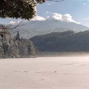Snowy lake with mountains in the background under a clear blue sky with few clouds