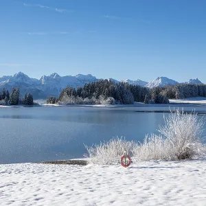 Snowy lakeside landscape with mountains in the background and clear sky