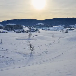 Snowy landscape with farms, rolling hills and mountains in the sunlight Snowy landscape with farms, rolling hills and mountains in the sunlight