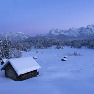 Snowy landscape with huts and forests in front of a mountain panorama in the soft light of the morning at Geroldsee