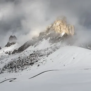 Paysage de montagne enneigé avec des nuages dramatiques et le soleil éclairant les sommets escarpés.