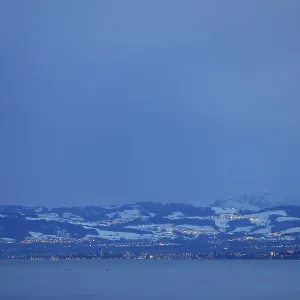 Snowy mountain landscape at dusk with view of lake and city lights