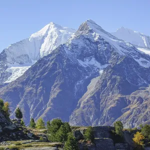 Snowy mountain peaks with rocks in the foreground under clear sky
