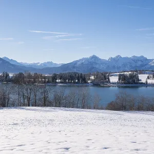 Snowy shore with a view of a quiet lake and mountains under a clear sky