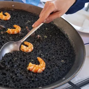 A spoon serving black rice with prawns and squid A spoon serving black rice with prawns and squid