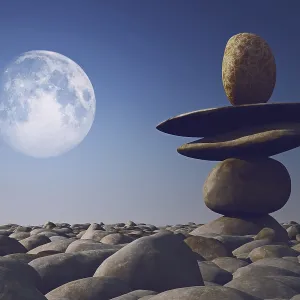 Stacked stones in sunlight with moon in sky on pebble sea beach Stacked stones in sunlight with moon in sky on pebble sea beach