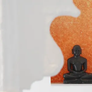 Statue of a black Buddha sitting meditating against an orange background Statue of a black Buddha sitting meditating against an orange background
