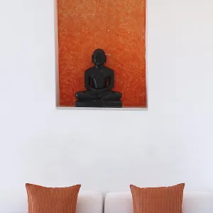 Statue of a black Buddha sitting meditating against an orange background Statue of a black Buddha sitting meditating against an orange background