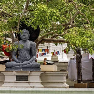 Stone Buddha under trees with decorative prayer flags in the temple area Stone Buddha under trees with decorative prayer flags in the temple area