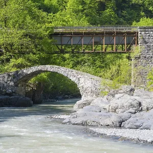 Stone and car bridge crossing a river in a mountainous forest landscape