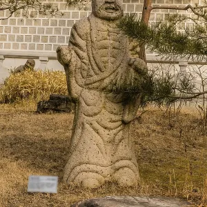 Stone carved statue of Buddhist deity kanakavatsa in front of white wall in garden in South Korea Stone carved statue of Buddhist deity kanakavatsa in front of white wall in garden in South Korea