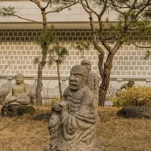 Stone carved statue of Buddhist deity vajraputra in front of white wall in garden in South Korea