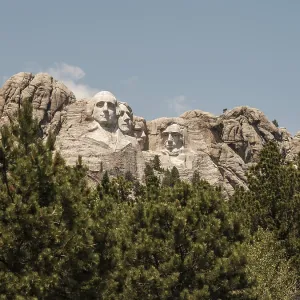 Stone carvings of presidents on Mount Rushmore with trees in the foreground under a clear blue sky