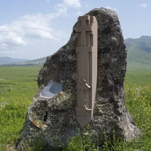 Stone with cross relief in front of a vast green landscape and blue sky Stone with cross relief in front of a vast green landscape and blue sky