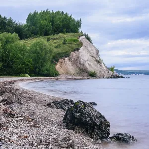 Stone on the riverbank and cliff with birch woodland on background