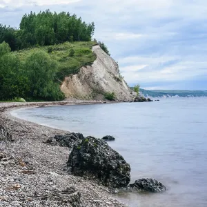 Stone on the riverbank and cliff with birch woodland on background
