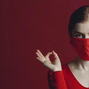 Studio portrait of young woman in protective medical face mask isolated on red background Studio portrait of young woman in protective medical face mask isolated on red background