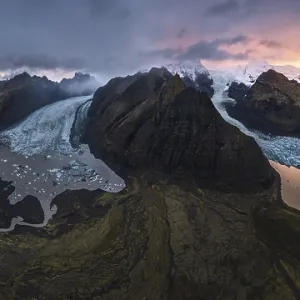 Vue aérienne impressionnante d'un glacier s'écoulant entre des montagnes volcaniques en Islande.