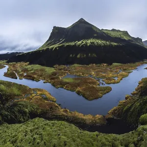 Vue panoramique impressionnante d'une montagne volcanique recouverte de mousse avec une rivière sinueuse et des marécages colorés dans les Hautes Terres islandaises, mettant en valeur la beauté naturelle dramatique et non touchée.