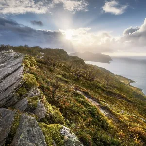 Sun breaks through dramatic clouds on the fjord with rocks and coloured moss in autumn