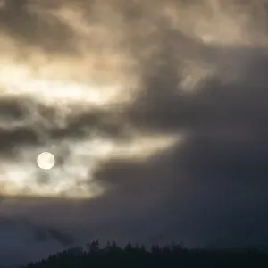 Sun above a mountain range breaking through morning clouds and fog Sun above a mountain range breaking through morning clouds and fog