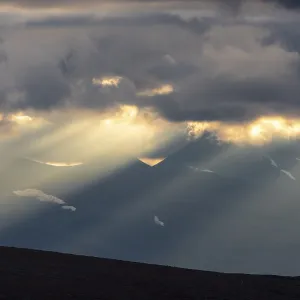 Sun rays fall through clouds in mountain landscape Sun rays fall through clouds in mountain landscape