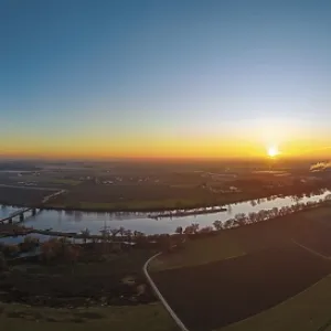 The sun sets over the Danube. The countryside is green with fields and trees The sun sets over the Danube. The countryside is green with fields and trees