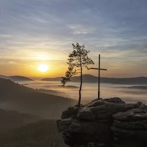 Sunrise with fog, peak with cross and tree on a sandstone rock