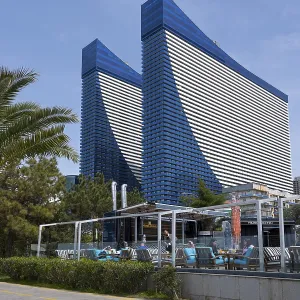 Two tall blue buildings with modern architectural features and a terrace in an urban environment