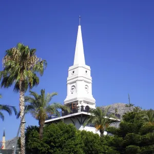 A tall white clock tower surrounded by palm trees