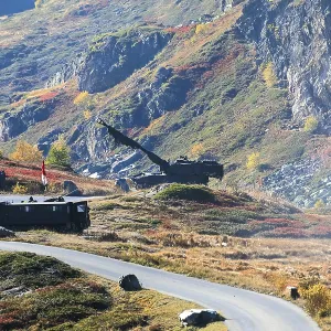 Tanks on a road through colorful autumnal hills in front of rocky mountains