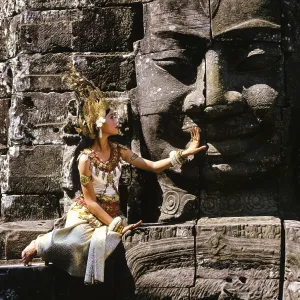 Temple dancer or apsara sitting in front of a face tower at Bayon Temple Temple dancer or apsara sitting in front of a face tower at Bayon Temple