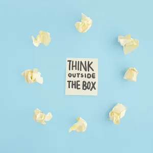 Think outside box text adhesive note surrounded with yellow crumpled paper blue backdrop