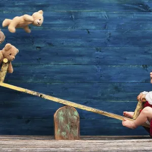 Three-year-old girl with teddy bear on seesaw