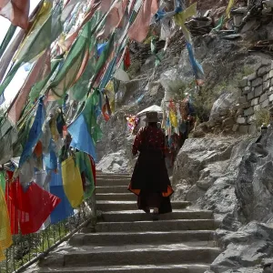 Tibetan Buddhism, Tibetan performing a Kora pilgrimage walk along stairs under colourful flags Tibetan Buddhism, Tibetan performing a Kora pilgrimage walk along stairs under colourful flags