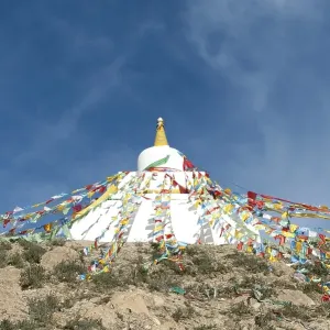 Tibetan Buddhism, white stupa with colorful prayer flags against a blue sky Tibetan Buddhism, white stupa with colorful prayer flags against a blue sky