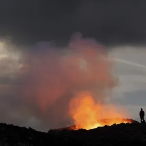 Tourists in front of reddish illuminated smoke cloud