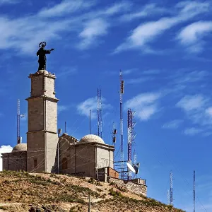 Tower with statue and antennae on a hill under a clear blue sky