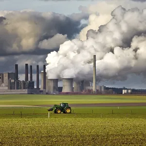 Tractor on a field in front of the steaming lignite-fired power station Frimmersdorf