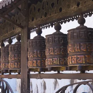 Traditional, artfully designed metal prayer wheels are placed in a row and are touched by hands Traditional, artfully designed metal prayer wheels are placed in a row and are touched by hands