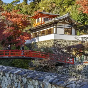 A traditional Japanese temple with red bridge and autumn foliage in a natural setting