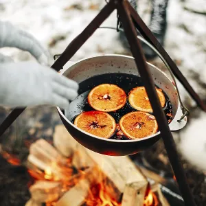 From above traditional mulled wine with slices of orange preparing in pot over burning logs in winter in countryside