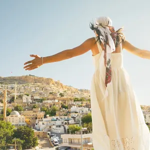 Traveler woman in white dress arms outstretched looking over panoramic view of historic city of Mardin Turkey with