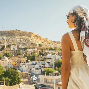 Traveler woman in white dress looking over panoramic view of historic city of Mardin Turkey with mosque minarets