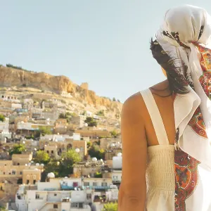 Traveler woman in white dress looking over panoramic view of historic city of Mardin Turkey with mosque minarets
