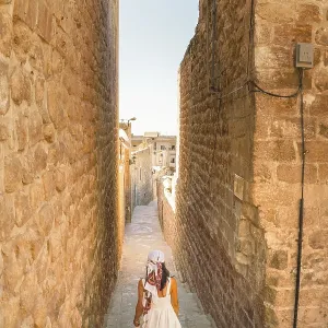 Traveler woman in white dress walking through narrow stone alley in historic city of Mardin Turkey with traditional