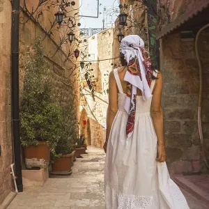 Traveler woman in white dress walking through narrow stone alley in historic city of Mardin Turkey with traditional