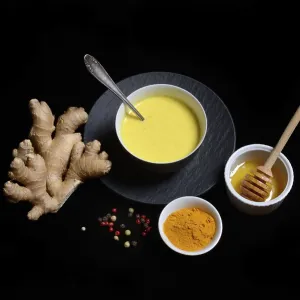 Turmeric milk in bowl, turmeric powder and ginger bulb