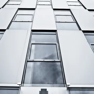 Upward view of a modern building with glass windows reflecting the cloudy sky